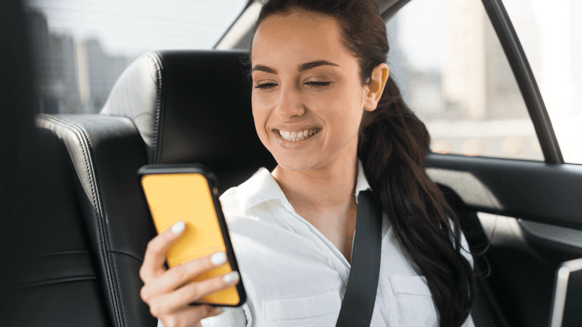Mulher no banco traseiro de carro de aplicativo usando celular amarelo da plataforma 99