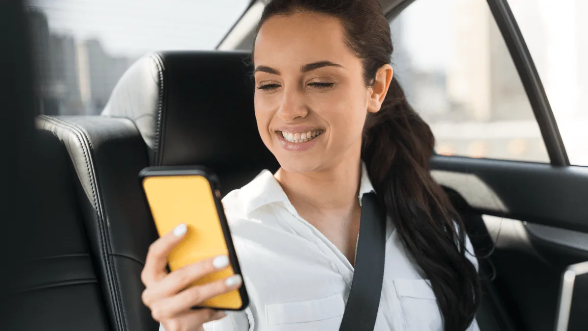 Mulher no banco traseiro de carro de aplicativo usando celular amarelo da plataforma 99