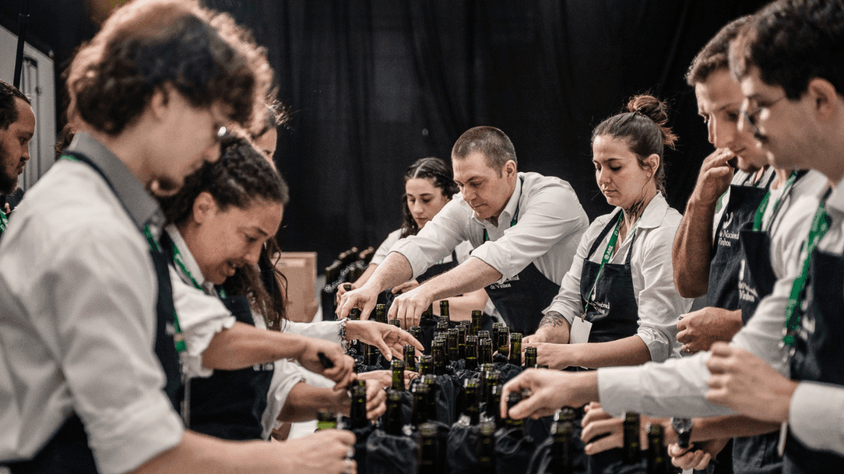 Mesa com garçons servindo vinhos e garrafas durante evento relacionado à Avaliação Nacional de Vinhos – Safra 2026.