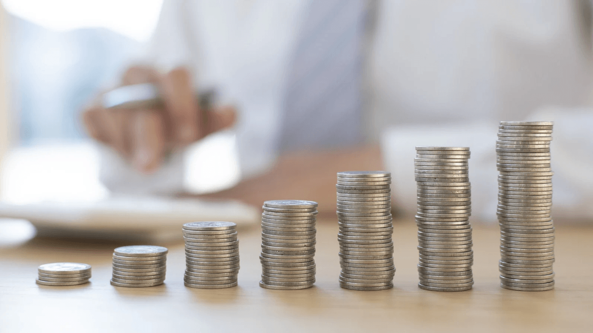 Moedas organizadas em pilhas crescentes sobre mesa executiva com planilhas financeiras.